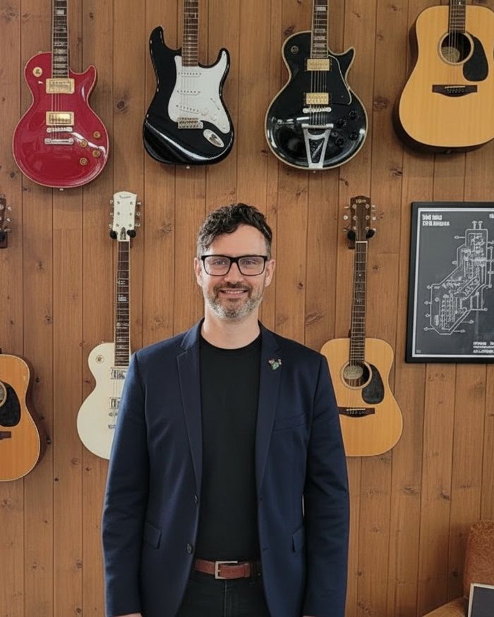 Matthew Rowan standing in front of a wall of guitars